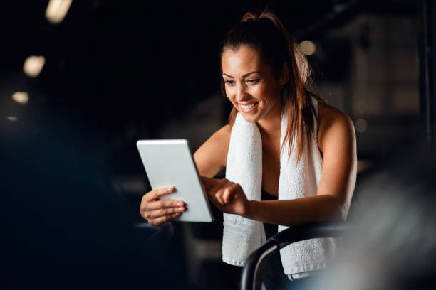молодая спортивная женщина с помощью цифрового планшета во время тренировки в тренажерном зале. - exercising sport gym spinning стоковые фото и изображения