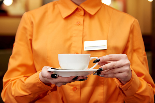 Service staff in orange shirt with a cup of coffee.