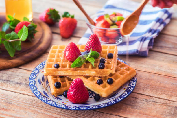 honig auf frische waffeln mit früchten gegossen - waffle syrup pouring breakfast stock-fotos und bilder