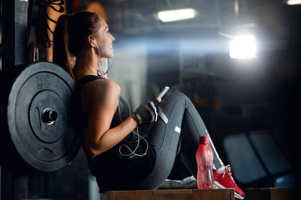 joven mujer atlética descansando después de entrenar deportes y escuchar música en un gimnasio. - body building exercises audio fotografías e imágenes de stock