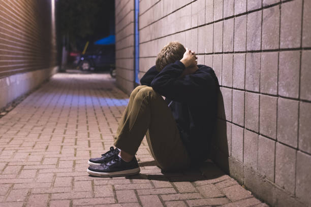 Sad teenager sitting in an alleyway. stock photo