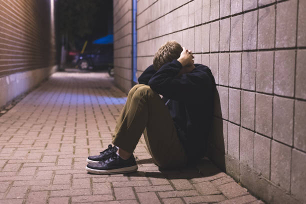 Sad teenager sitting in an alleyway. The image displays a sad teen boy sitting in an alleyway all alone at night. child crimes stock pictures, royalty-free photos & images