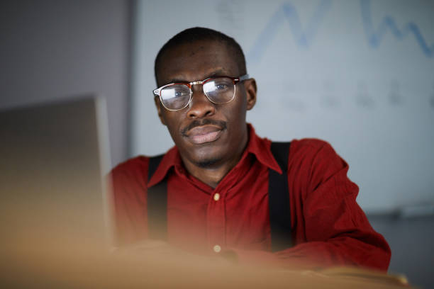 Portrait of modern African businessman looking at camera while  working in dark office, copy space