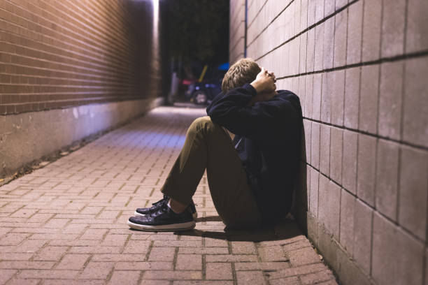 Sad teenager sitting in an alleyway. stock photo