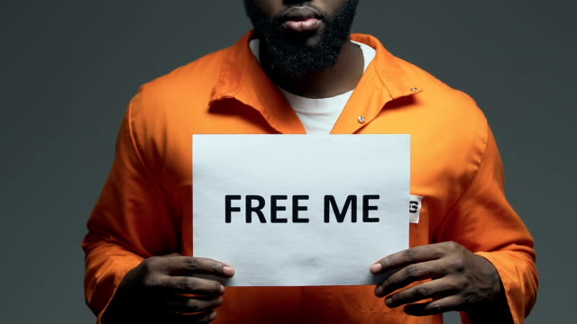 Free me phrase on cardboard in hands of Afro-American prisoner, amnesty asking