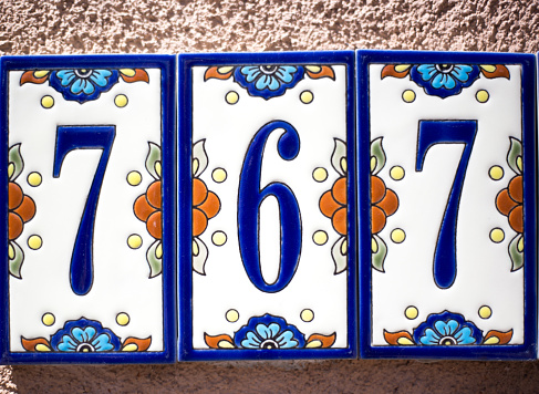 Ceramic Number 767 Street Address; Colorful Mexican floral tiles on adobe wall.