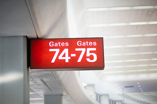 A low angle view of a sign showing gates 74-75 at the airport. The sign glows with a deep red color as the numbers stand out in white.