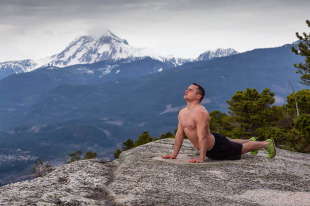 Fit and Muscular Young Man is doing exercises on top of the Mountain during a cloudy day. Taken on Chief Mountain in Squamish, North of Vancouver, BC, Canada.