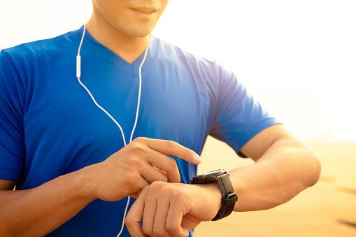 young Man running on beach and checking Heart Rate Monitor On watch