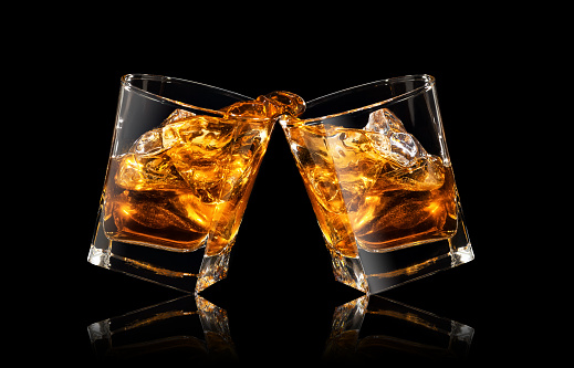 glasses of whiskey making toast with splashes on black background