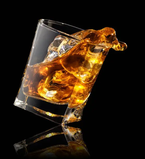 splash of whiskey with ice cubes in glass on black background
