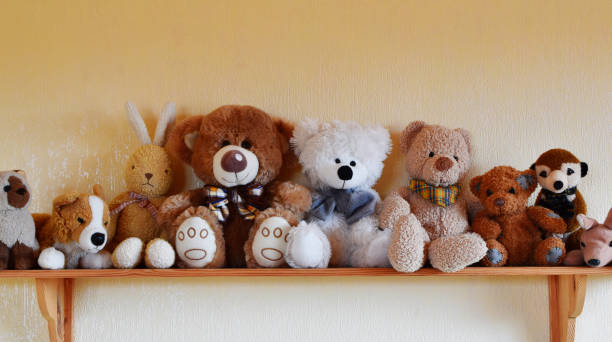 Toys for children sitting in row on wooden shelf Soft plush toys for children sitting in row on wooden shelf, different toy animals for kids on yellow wall background with copy space. stuffed toy stock pictures, royalty-free photos & images