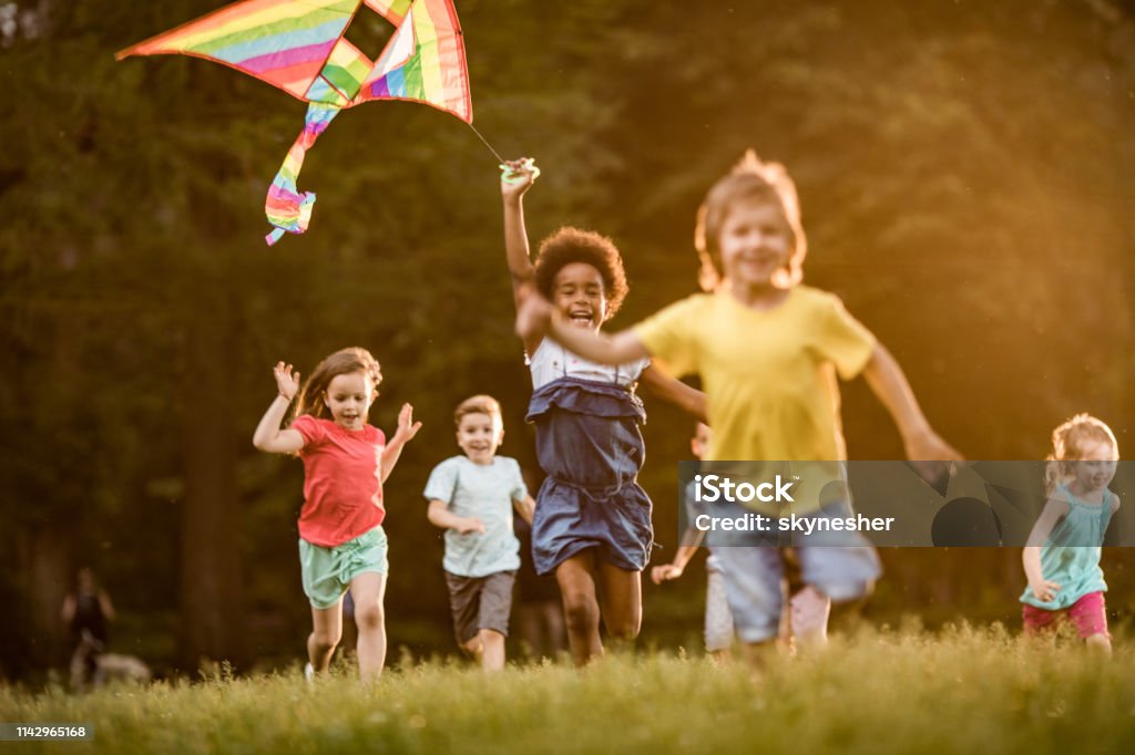 Happy kids playing with kite in springtime at the park. Group of happy kids having fun while running with a kite during spring day at the park. Child Stock Photo