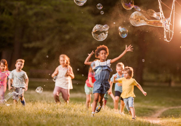 istock Group of kids having fun while catching rainbow bubbles in springtime. 1142965469