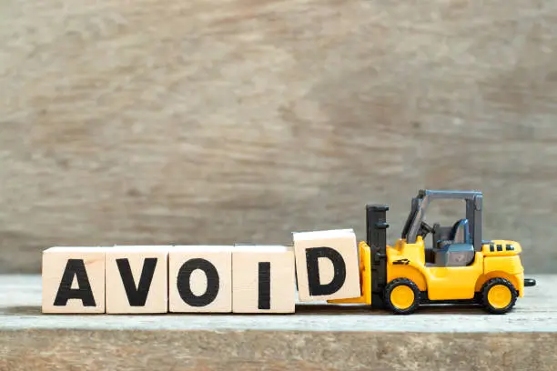 Toy forklift hold letter block d to complete word avoid on wood background