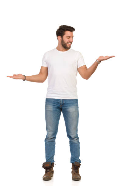jeune homme en jeans et t-shirt blanc est debout et comparer quelque chose. - arms outstretched arms raised studio shot adult photos et images de collection