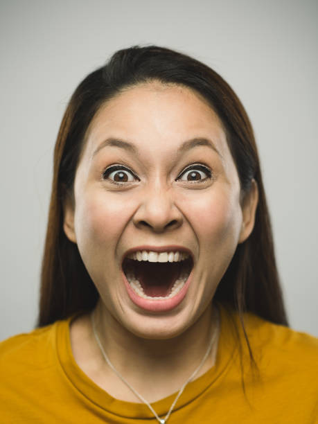 Portrait of real malaysian young woman with shouting expression Close up portrait of asian young woman with shouting expression against  white gray background. Vertical shot of malaysian real people screaming in studio with long brown hair. Photography from a DSLR camera. Sharp focus on eyes. women screaming surprise fear stock pictures, royalty-free photos & images