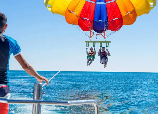 Photo of Happy couple Parasailing on Miami Beach in summer. Couple under parachute hanging mid air. Having fun. Tropical Paradise. Positive human emotions, feelings, family, travel, vacation.