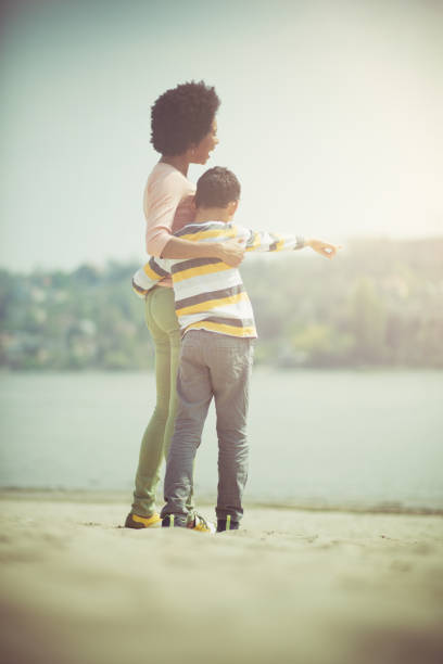 Young European mother holds her six-year-old dark-skinned daughter in her arms. Happy hugs on the beach on a summer day. Lifestyle concept.