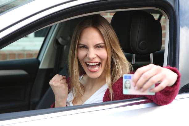Happy woman is delighted with the passing driving test and shows off her driver's license Happy woman is happy about the passed driving test and shows her driver's license drivers license stock pictures, royalty-free photos & images