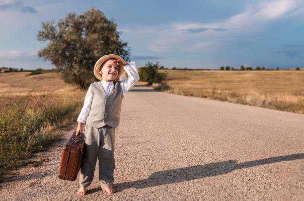 Beautiful winter photo of a little warmly dressed girl with a shadow on a rural asphalt winter road without snow, rear view