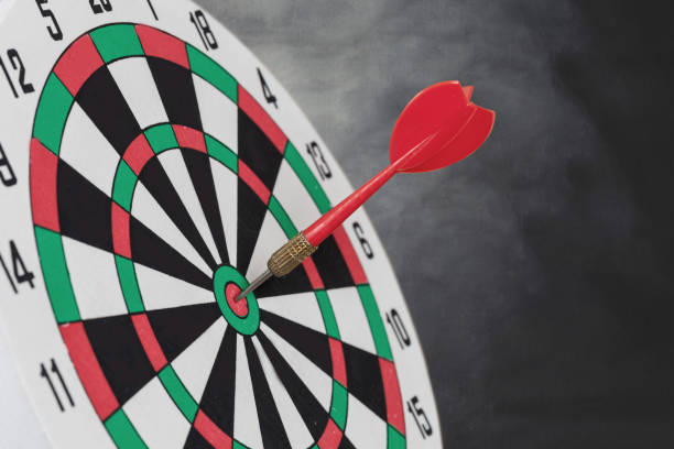 istock Dart arrow hitting in bullseye on dartboard with black background. 1142996705