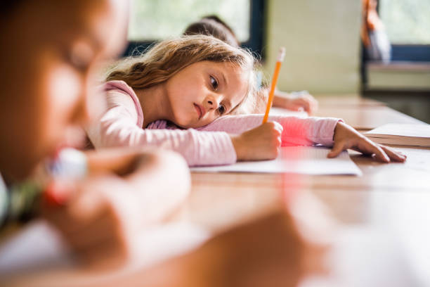 Exhausted elementary student writing in a notebook during a class in the classroom.