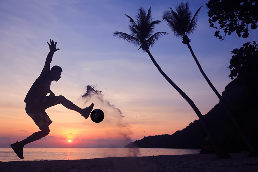 Silhouette Volley Kick football on the beach, Asian man play soccer at sunrise early morning.