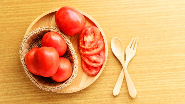 istock Fresh and slice tomatoes placed on a wooden plate. Spoon and fork lay on a wooden table. Cooking ingredient. Breakfast preparing and food background concept with copyspace. 1143007546