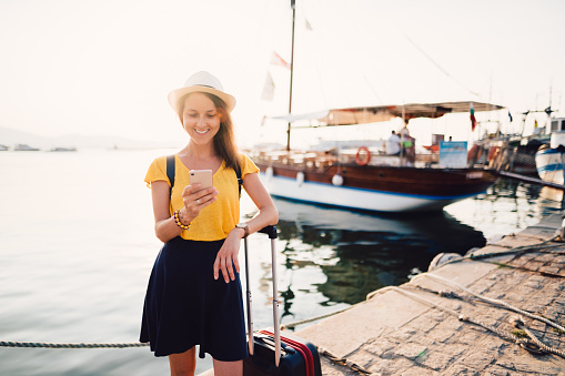 Tourist woman with suitcase at the marina ready for cruise trip