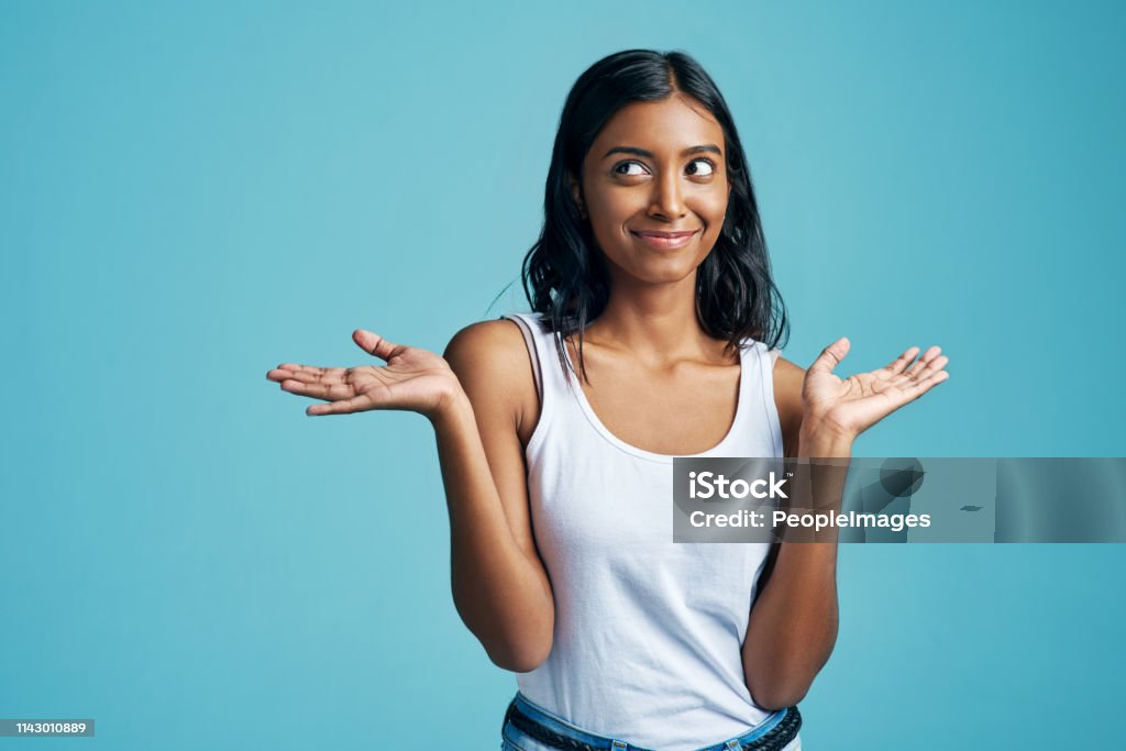Just a shrug of the shoulders Studio shot of a beautiful young woman shrugging her shoulders against a blue background Women Stock Photo