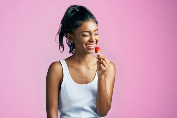 She's enjoying that strawberry Studio shot of a beautiful young woman eating a strawberry against a pink background 1 STRAWBERRY stock pictures, royalty-free photos & images