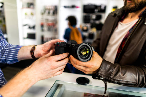 Camera store seller showing various camera lenses on a mirrorless camera to his customer in a camera accessories store.