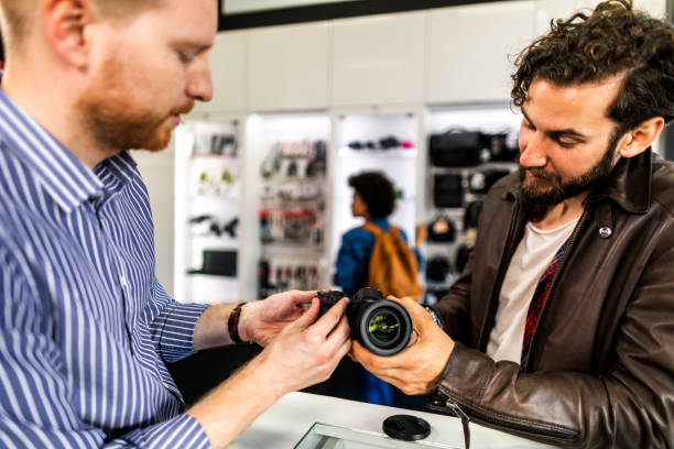 istock Camera store seller showing various camera lenses on a mirrorless camera to his customer in a camera accessories store 1143013227