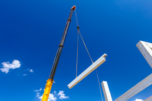 Mobile crane is operating with a huge concrete joist that hangs on chain.