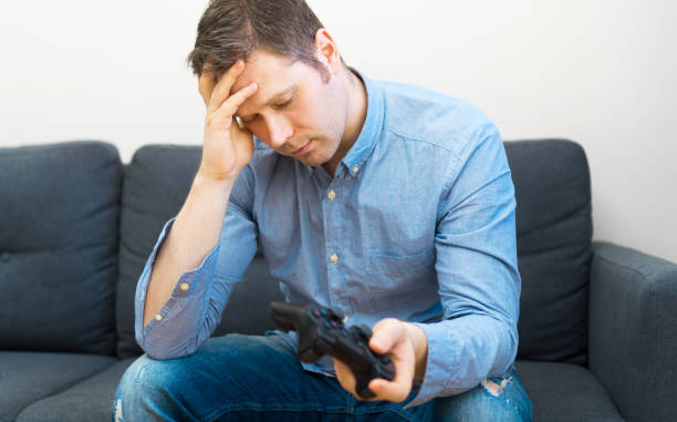 istock Sad man with gamepad in hands playing video game. 1143016626