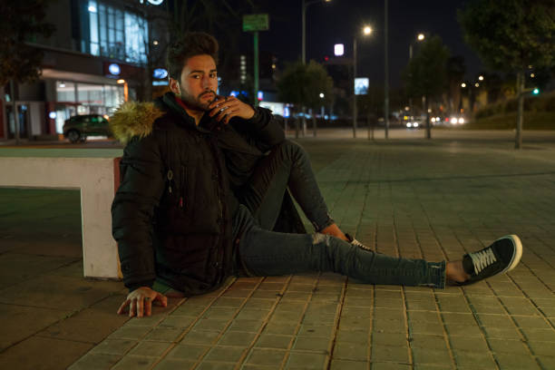 Stylish young man sitting on a the sidewalk at night