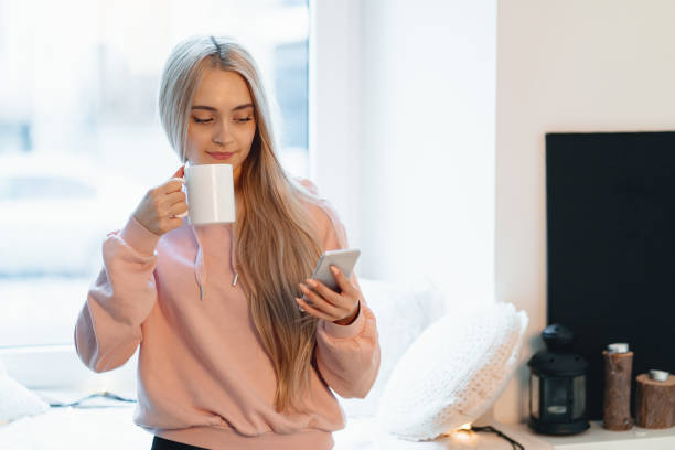 istock Pretty young woman enjoying coffee while using a smartphone by the windows indoors 1143017332