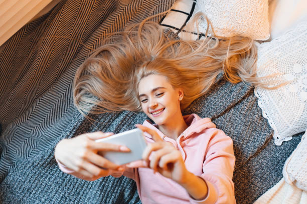 istock Pretty young girl having fun, making selfie with smart phone while lying on the bed at home 1143017366