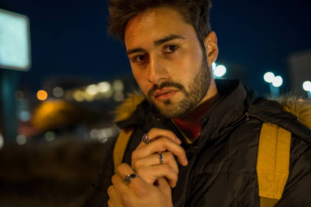 Cool young man crossing the street at night, lighted by color city lights.