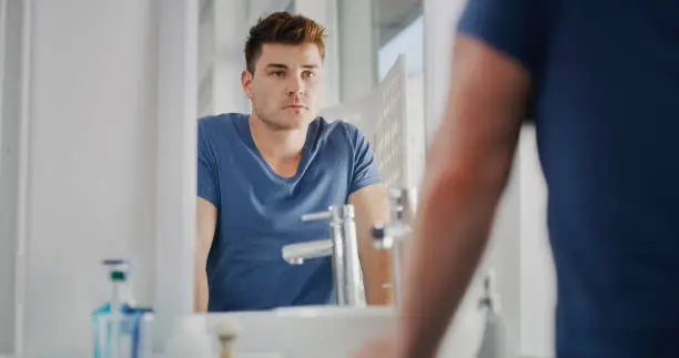 Cropped shot of a handsome young man going through his morning routine in the bathroom at home