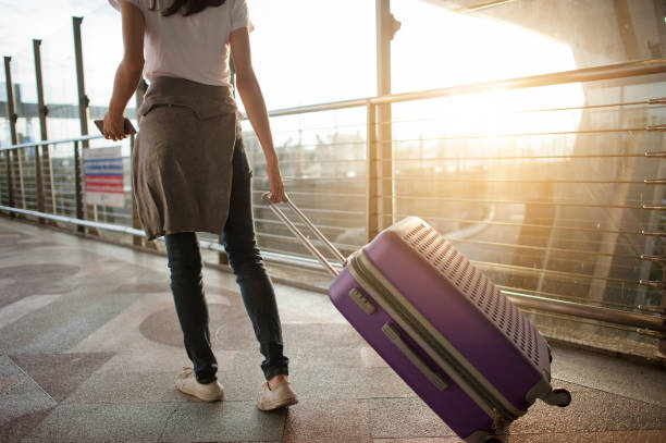 istock Young woman pulling suitcase in modern airport terminal. Travelling guy with his luggage while waiting for transport. Rear view. Copy space 1143024754