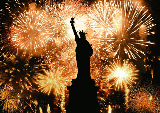 silhoute of the Statue of Liberty lit at night by fireworks as holiday celebration stock photo