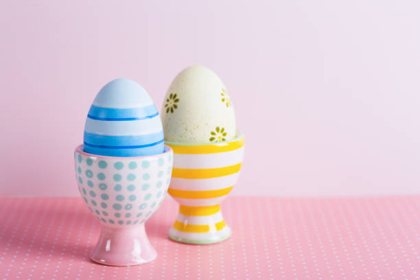 istock Closeup two colorful painted Easter eggs in vibrant modern egg stands on pastel pink background. 1143029289
