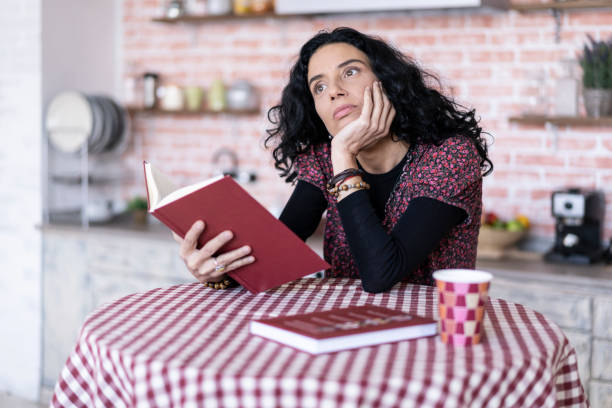 istock Woman sitting in kitchen and reading a book 1143029796