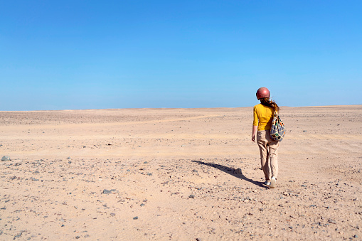 Rear view of a woman with protective helmet walking Sahara desert alone.