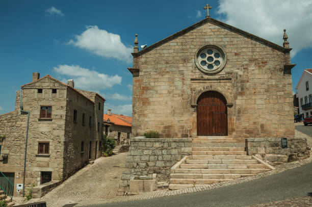 Medieval church with stone wall and wooden door next to old houses in a deserted alley, on a sunny day at Monsanto. Considered one of the cutest and most peculiar historic village of Portugal.