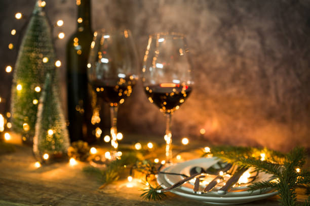 primo piano di vino rosso in tavola con luci natalizie. tavola di natale e albero. - cena natale foto e immagini stock
