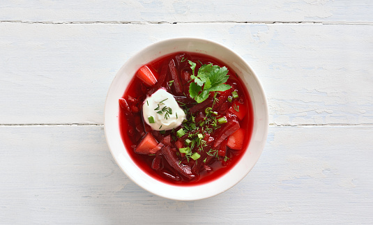Bowl of beetroot soup with greens and sour cream on white wooden background with copy space. Top view, flat lay