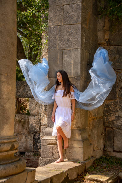 um retrato de uma menina com cabelo marrom longo com um lenço de seda branco que está por uma coluna antiga em um lugar histórico. - hamat gader - fotografias e filmes do acervo